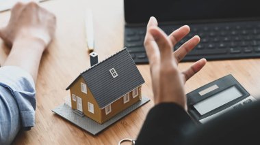 Gayrimenkul acentesinin modern ahşap masada ev sahipliği için yapılan anlaşma / internet harcamalarını müşterisine açıklamak için dizüstü bilgisayarı kullanması. Emlakçı / Komisyoncu / Menajer / Dağıtıcı kavramı.