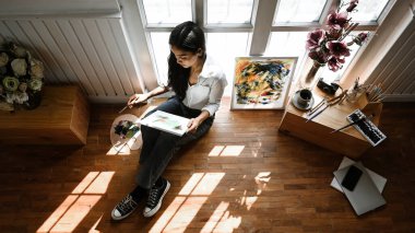 Genç sanatçı kız kanvas çizerken / çizerken pencerelere yaslanır / odaklanır.