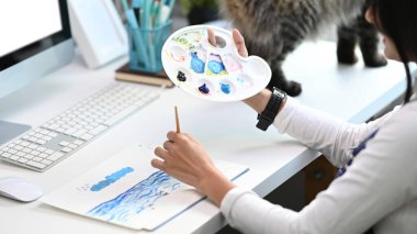 Elinde palet olan sanatçı ya da tasarımcı kadının kağıda resim yapmasını kapat.