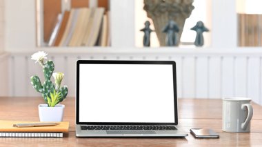 Beyaz ekranlı bilgisayar bilgisayarı, Kaktüs, Not Defteri, Kalem, Akıllı Telefon, Kahve fincanı düz bir şekilde arka planda rahat oturma odası rafı olan ahşap çalışma masasının üzerinde yatıyordu..