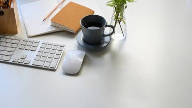 Kahve fincanı, klavye, fare, notalar, kalem ve saksı bitkisinin modern beyaz masa üzerinde bir araya getirilmesi. Düz ofis ekipmanları. Rahat iş yeri kavramı.