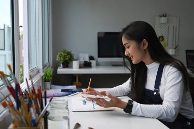 Sanat stüdyosunda önlüklü, resim yapan mutlu genç bir kadın ressam..
