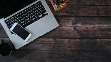 Dizüstü bilgisayarın üst görüntüsü, akıllı telefon ve ahşap masadaki defter. Metin iletisi veya bilgi içeriği için alanı kopyala.