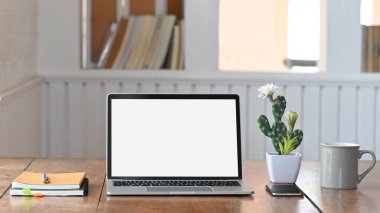 Tahta çalışma masasına koyulan beyaz ekran dizüstü bilgisayarın fotoğrafı kaktüs, kahve fincanı, defter ve akıllı telefon da dahil. Modern çalışma masası konsepti.