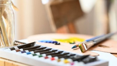 Seçici odak renkleri mürekkep tüpü boya fırçası, renk örnekleri ve boya fırçasını arka plan olarak bulanık sanatçı stüdyosunun bulunduğu vazoda bir araya getiriyor..