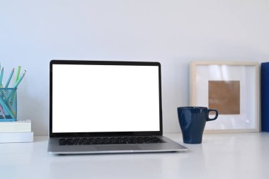 Boş ekran, kahve fincanı ve kitapları beyaz ofis masasına dizilmiş dizüstü bilgisayarı taklit et..