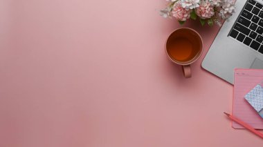 Dizüstü bilgisayarı, kahve fincanı, not defteri ve pastel pembe arka planda kopyalama alanı olan en küçük çalışma alanının üst görünümü.