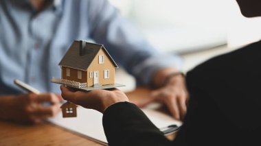 House broker 'ın, kağıt üzerine yazı yazarken ve ahşap masada anlaşma imzalarken örnek ev modelini elinde tuttuğu görüntüler. Kredi, Borç, Satma / Alma Anlaşması.