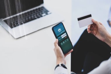 Akıllı telefon kullanan ve elinde kredi kartı tutan genç bir kadının çevrimiçi veya çevrimiçi banka ödemelerini yaparken görüntüsü kesilmiş..