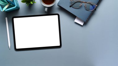 Dijital tablet, defter, mavi masadaki stil kalemle lüks çalışma alanının üst görünümü.