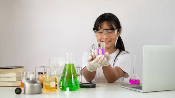 若いです可愛いです女の子で安全眼鏡と手袋を持っています化学のためのフラスコを保持しながら 隔離された白い背景を持つ現代の研究室で科学実験を行います — ストック写真