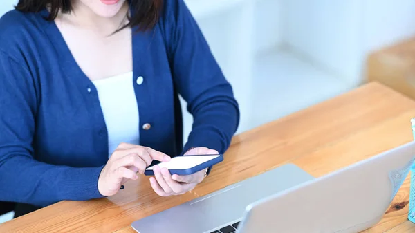 Young female using mobile phone checking email or social media at her workspace.