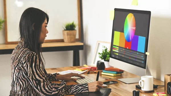 Creative designer sitting at wooden working desk using digital tablet for selecting color from color management/color palette program. Graphic design concept