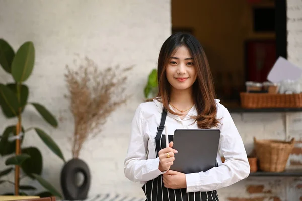 站在咖啡店时 快乐的年轻女性咖啡师拿着数码平板电脑 对着相机微笑 — 图库照片