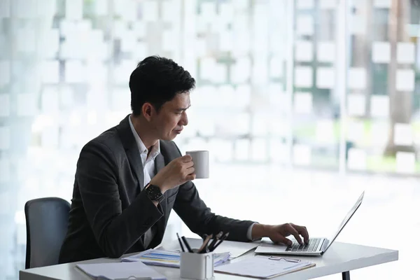 Elegancki Biznesmen Pijący Kawę Przewijający Informacje Online Laptopie Biurze — Zdjęcie stockowe
