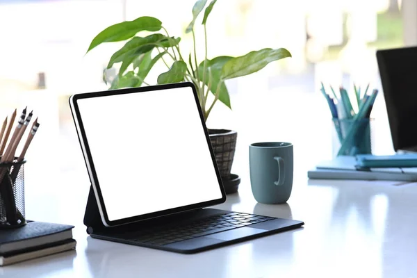 Graphic designer workstation with tablet computer, plant, stationery and coffee cup on white table.