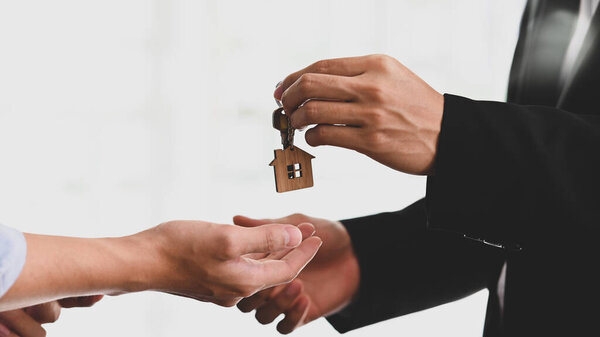 Cropped shot of Real estate agent giving a property's key to customer while standing at the orderly office.
