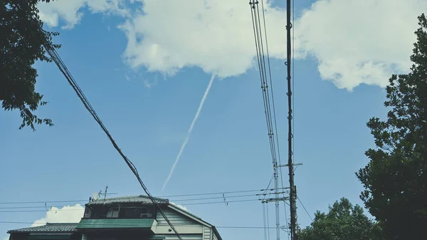 The roof apex and many crossing over cables running into the houses on the street with blue sky on a sunny day.