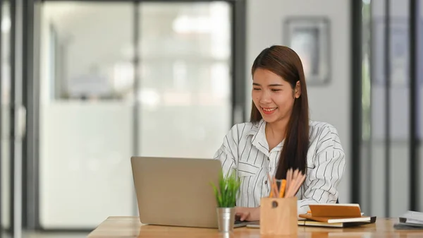 ビジネス女の子でストライプシャツタイプのラップトップと座っている木製の作業机で現代的なオフィスの背景 — ストック写真