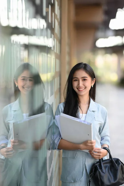 Portrait of asian businesswoman holding documents folder and  standing outside office building.