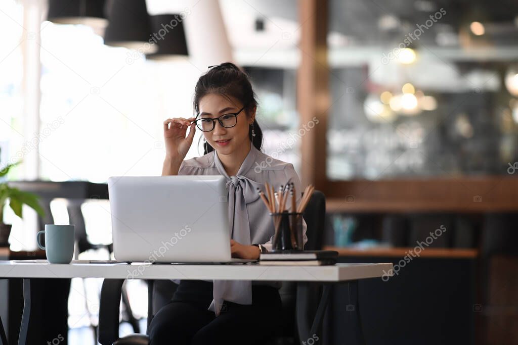 Businesswoman hand touching her spectacles and working on laptop at office.