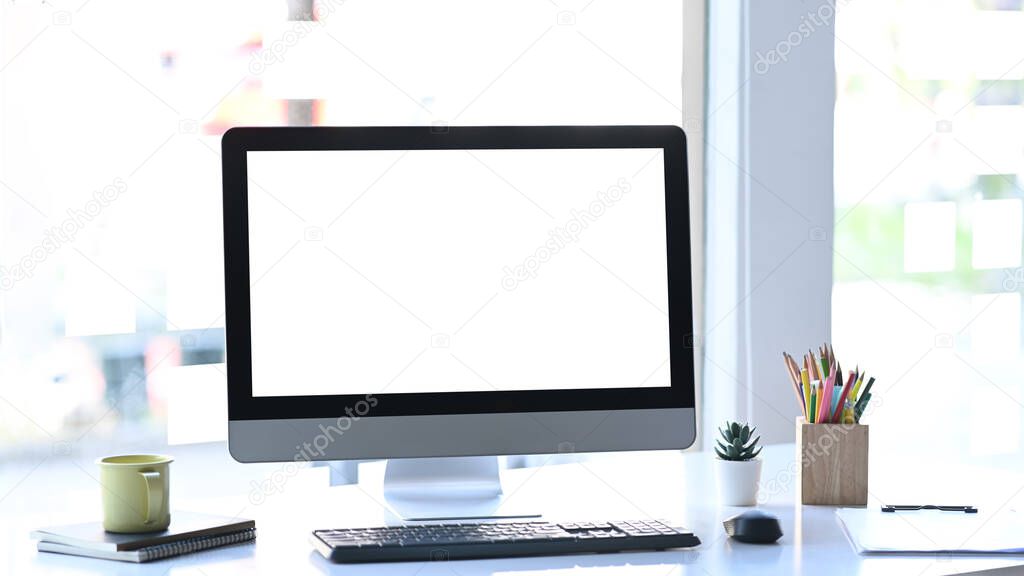 Stylish workstation with computer, coffee cup and office supplies on white table.