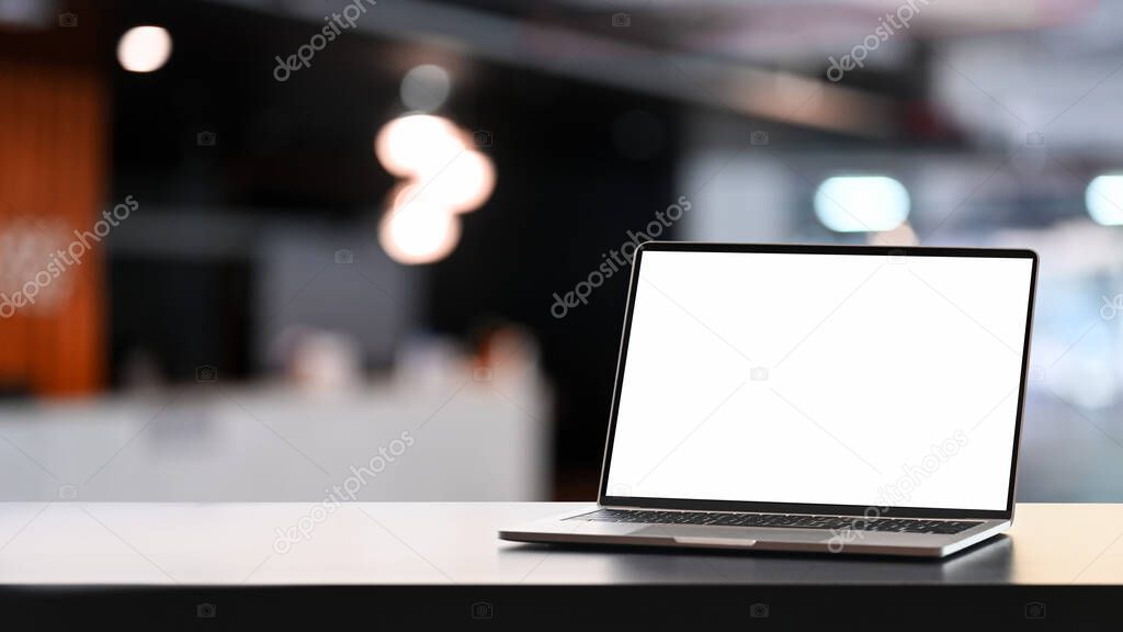 Open laptop computer with blank screen on white table and conference room blurred background.