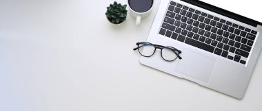 Bilgisayarın, gözlüklerin, kahve fincanının ve beyaz arkaplandaki kopyalama alanının yatay fotoğrafı.