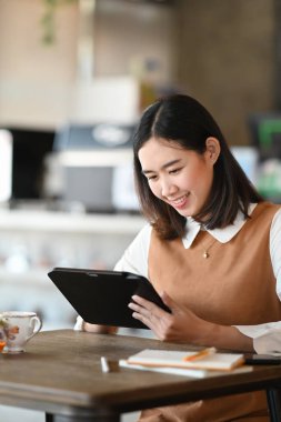 Dijital tablet kullanan ve kafede otururken gülümseyen genç bir kadının portresi..