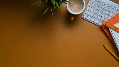 Üst görünüm klavye, not defteri, bitki, kahve kupalı sarı derili çalışma alanı. 