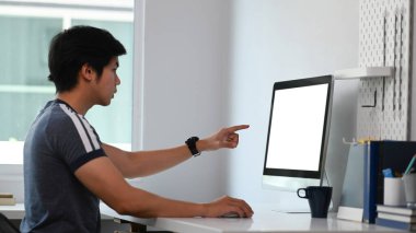 Ofiste oturan ve bilgisayar ekranını gösteren genç adamın yan görüntüsü.