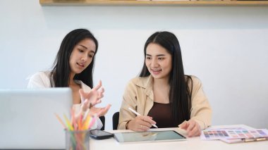 İki genç kadın grafik tasarımcısı ofiste iş projesinde birlikte çalışmayı tartışıyor..