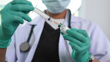 Koruyucu zaman maskeli bir doktorun elinde şırıngayla şişeden sıvı aşı alıp hastanede enjeksiyona hazırlandığı görüntüler..