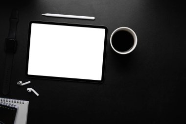 Boş ekranlı dijital tabletin üst görüntüsü, stilus kalem, kablosuz kulaklık ve koyu masa üzerinde kahve fincanı.