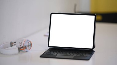 Boş ekran ve kulaklıklı bilgisayar tabletinin beyaz masadaki görünümünü kapat.