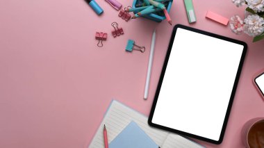 Dijital tabletli ofis masası, pembe arka planda buket ve kırtasiye malzemesi.