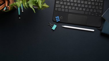 Kablosuz klavyesi, stilus kalemi, kahve fincanı, bitki ve fotokopi alanı olan modern koyu iş yeri..