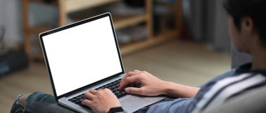 Evdeki kanepede otururken bilgisayarlı bilgisayar kullanan bir gencin yatay fotoğrafı..