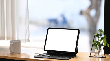 Bilgisayar tableti, kahve fincanı ve ahşap masadaki bitki ile rahat bir iş yeri..