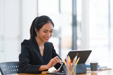 Modern ofiste otururken bilgisayar tabletine stilus kalem yazan neşeli bir kadın..
