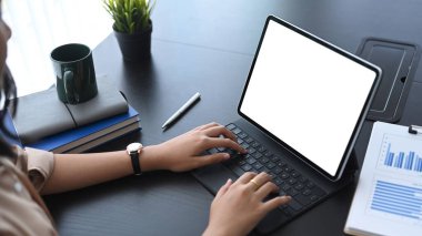 Genç iş kadını, modern işyerinde otururken tablet ekranda finansal verileri analiz ediyor.