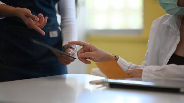 Koruyucu maske takan genç bir kadının modern kahve dükkanındaki garsonla tabletten sipariş verirken görüntüsü..