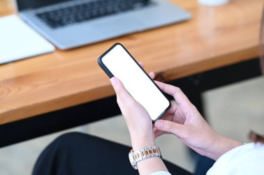 İş yerinde otururken cep telefonunu boş ekranla tutan genç bayanın görüntüsünü kapat.