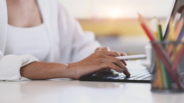 Close up view of hand of young female designer holding stylus pen and working on computer tablet.