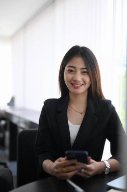 Meteor odasında dururken elinde akıllı bir telefon tutan ve kameraya gülümseyen genç iş kadını..