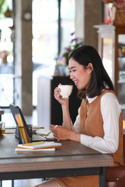 Bilgisayar tabletinde çalışan ve kahve içerken kahve içen genç bir kadının portresi..