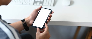 Genç adamın, iş yerinde otururken boş ekranla akıllı telefonu taklit edişinin yakın görüntüsü..