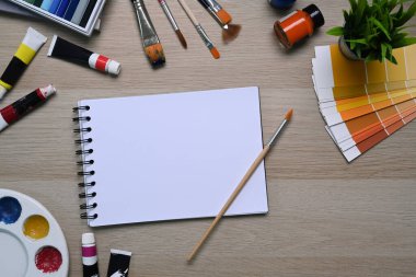 Sanatçı çalışma alanı boş defter ile çevrili renk örnekleri, boya fırçaları ve diğer çeşitli ekipmanlar ahşap arka planda.