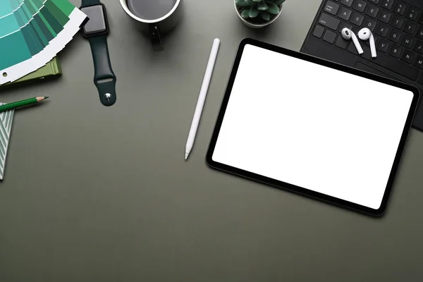 Top view of creative workplace with smart watch, mobile phone , wireless keyboard, color swatches, earphone and copy space on green table.