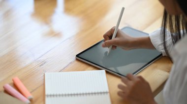 Yaratıcı bir kadının el ele tutuşması / bir stilus kalem kullanarak çalışma masasını rahat oturma odasının üzerine koyan beyaz boş ekran bilgisayar tabletini arka plan olarak çizmek için kesilmiş görüntüsü.